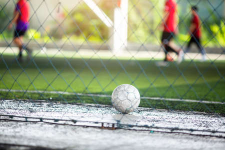 Soccer ball on floor in Indoor soccer field with blurry soccer player and mesh. Sport background.の写真素材