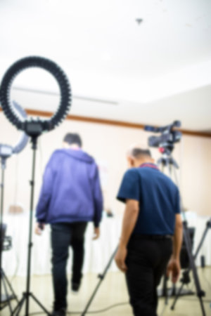 Blurry image of cameramans working with camera and blurry ring lighting in studio for broadcasting. Mass media concept.の写真素材