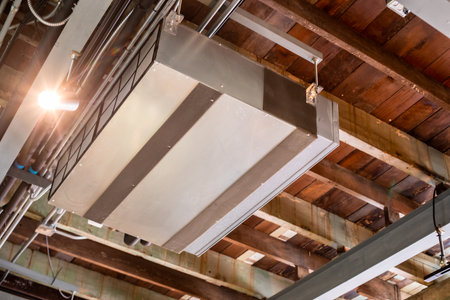 Selective focus to Ceiling mounted cassette type air condition units with other parts of ventilation system with hanging lights and other construction parts in vintage office or vintage shop.の写真素材