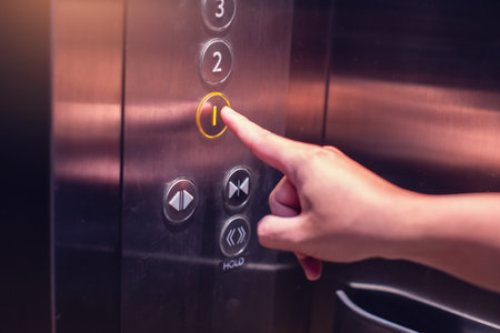 Selective focus on forefinger pressing on button in the passenger lift. Close up of elevator control panel in building. Passenger elevator cabin presses floor selection button. Knob with Bell alphabetの写真素材