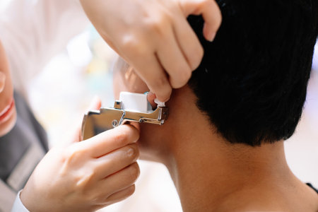 Selective focus to face of Asian young boy doing ear piercing procedure. Doctor hands hold ear...