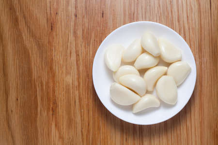 Peeled garlic in a white plate on wooden table. Top view.の写真素材