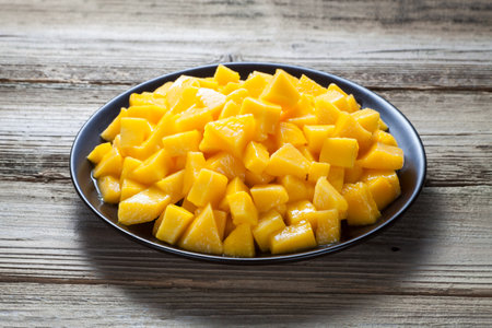 Diced mango in a black plate on old wood.の写真素材