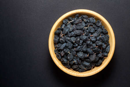 Black currant raisins in a wooden bowl on black background. Top view.の写真素材