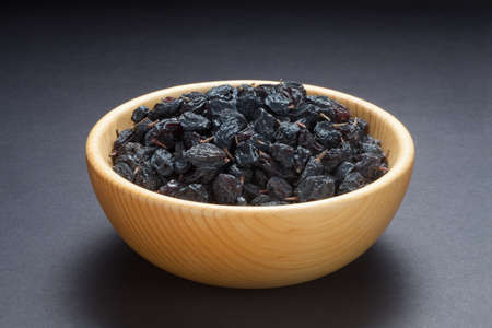Black currant raisins in a wooden bowl on black background.の写真素材