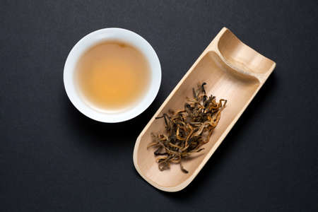 A cup of Yunnan black tea with dry tea leaves on black background. Top view.の写真素材