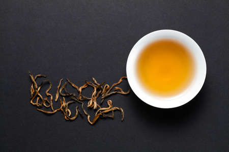 A cup of Yunnan black tea with dry tea leaves on black background. Top view.の写真素材