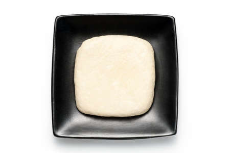 A piece of fresh tofu on a black plate on white backgorund.
