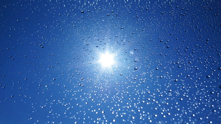 Watter drops on window with blue sky and sun lightの写真素材