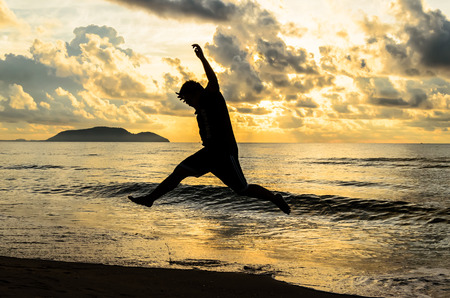 Happy man jumping on the beach at dawn.の写真素材