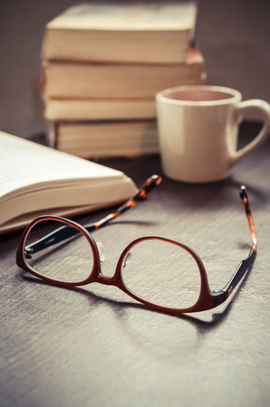 Vintage old books and glasses with a cup of coffee on wooden deck tabletop against grunge wallの写真素材