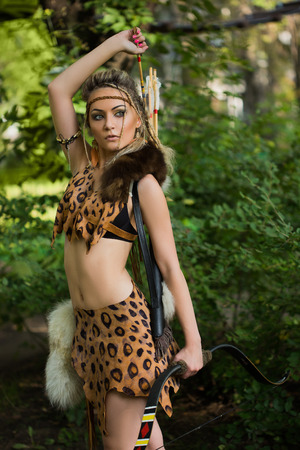 Beautiful amazon woman posing with bow in green forestの写真素材