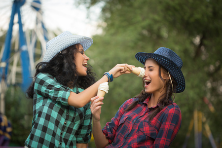 two beautiful girls in cowboy hats eating ice cream. amusement parkの写真素材