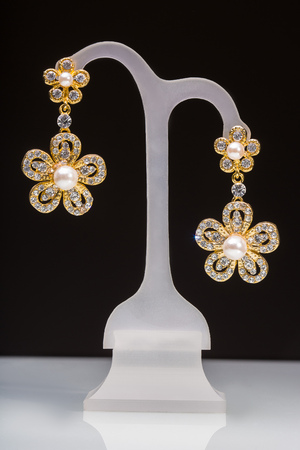 gold earrings with white little stones isolated on a black background. in the form of flowersの写真素材