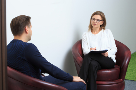 Female psychologist consulting pensive man during psychological therapy sessionの写真素材