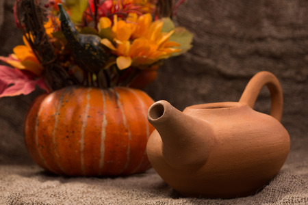 earthenware teapot with a decorative pumpkin on a background of burlapの写真素材