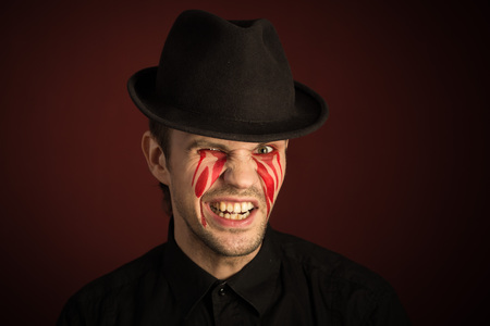 portrait of a man with bloody tears on burgundy backgroundの写真素材