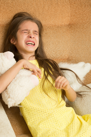 little girl crying on a chair. soft toyの写真素材