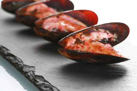 mussels in their shell on a black slate plate. with sauce