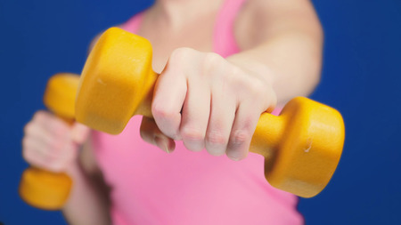 A woman in a pink T-shirt with a deep neckline is boxing dumbbells. focus on dumbbells, body blurry. copy space.の写真素材