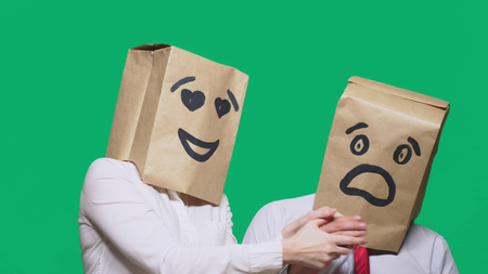 concept of emotions, gestures. a couple of people with bags on their heads, with a painted emoticon, a smile, eyes in love, and the second with a mask of fright, fear. sexual harassment concept.の写真素材