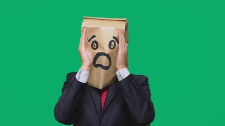 concept of emotions, gestures. a man with paper bags on his head, with a painted emoticon, fear. talking on a cell phone.の写真素材