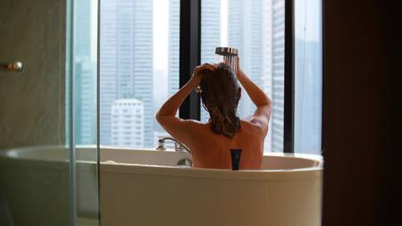 Beautiful Woman enjoying relaxing bath in luxury bathroom with a window. Lifestyle and beauty care concept. view from the window to the skyscrapersの写真素材