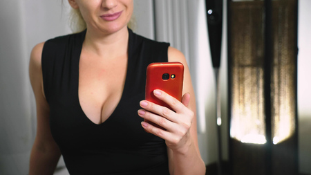 Beautiful girl use a cellular smartphone while sitting in the living room in the evening. Happy smiling young woman chatting on the internet at homeの写真素材