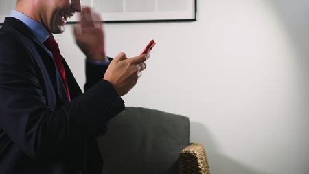 Beautiful gay use a cellular smartphone while sitting in the living room in the evening. Happy smiling young man chatting on the internet at homeの写真素材