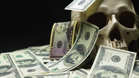human skull in a pile of American currency on black background