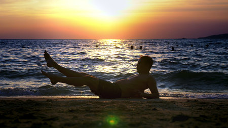 Playful handsome guy in shorts doing fitness, on the seashore against the backdrop of a wonderful sunset.の写真素材