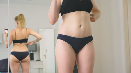 The concept of overweight and weight loss. A woman looks at herself in the mirror and photographs her figure. to compare the results before and after losing weightの写真素材