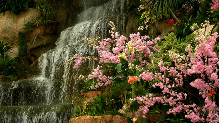 a large artificial waterfall framed by pink flowers and green leavesの写真素材