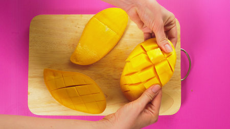 top view, female hand cuts fruit with a knife on a wooden board, mango. The concept of natural...