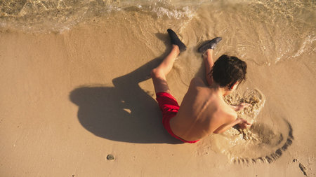 teenage boy building sand castle on tropical beach.の写真素材