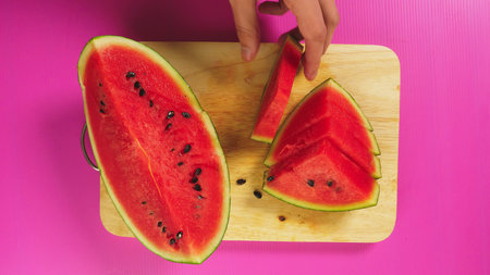 top view, female hand cuts fruit with a knife on a wooden board, red watermelon. The concept of natural healthy foodの写真素材
