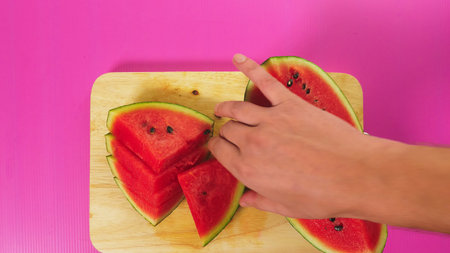 top view, female hand cuts fruit with a knife on a wooden board, red watermelon. The concept of natural healthy foodの写真素材