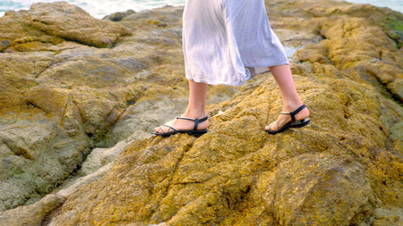 close-up. women's legs in sandals and a long gray skirt are on the rocky seashore at low tideの写真素材