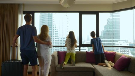 happy family, woman, man and two children with a suitcase on the background of skyscrapers in a panoramic windowの写真素材