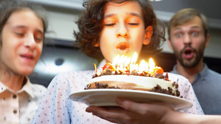 Happy smiling boy blowing candles on her birthday cake. children surrounded by their family....