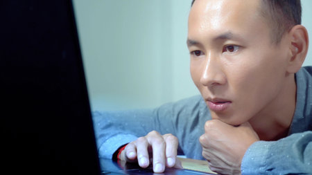 Young handsome asian man using his laptop, sitting at desk in officeの写真素材