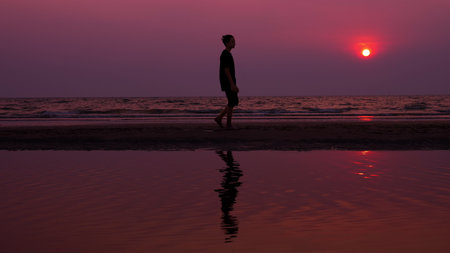 silhouette. lonely asian young man walking peacefully along a deserted beach at sunset. seascapeの写真素材