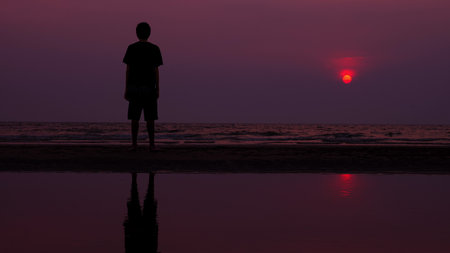 silhouette. lonely asian young man walking peacefully along a deserted beach at sunset. seascapeの写真素材