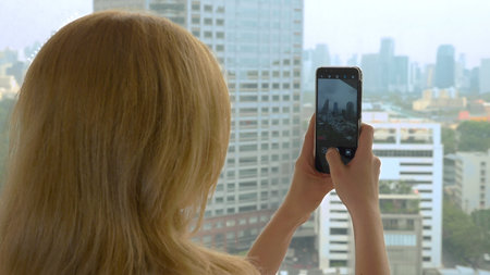 Elegant blonde woman making a photo on the phone. woman photographs the view from the window of the skyscrapersの写真素材