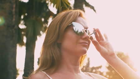Beautiful stylish blond woman in sunglasses , walking along a palm tree path. The palm is reflected in the glasses.の写真素材