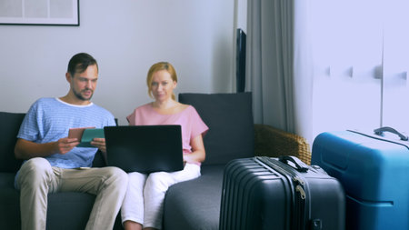 The concept of tourism, online shopping tours. Romantic couple preparing to travel at home. Sit on the couch with a laptop and passports in their hands. while the suitcases are close by, focus on the suitcasesの写真素材