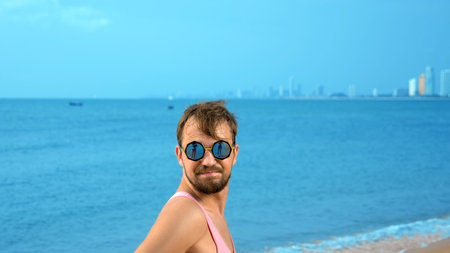 Close-up, Playful handsome guy in pink t-shirt on a tropical beach. he looks at the camera, rejoices...