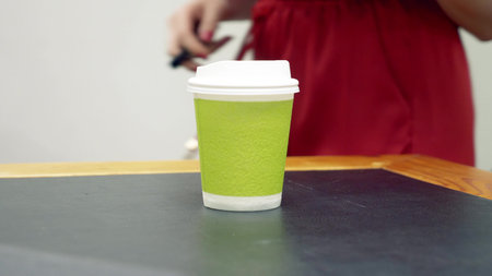 A woman in a red dress takes a cardboard cup of coffee and puts lip gloss next to it.の写真素材