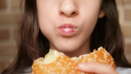 close. childs mouth. girl eating a hamburgerの写真素材