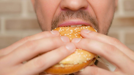mouth close up. man bites off a piece of hamburgerの写真素材